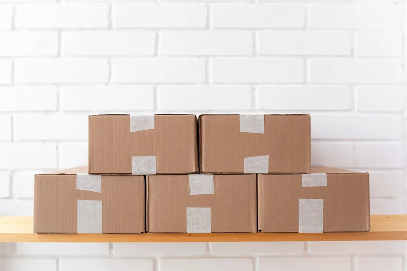 Stack of taped cardboard parcels against a white brick wall