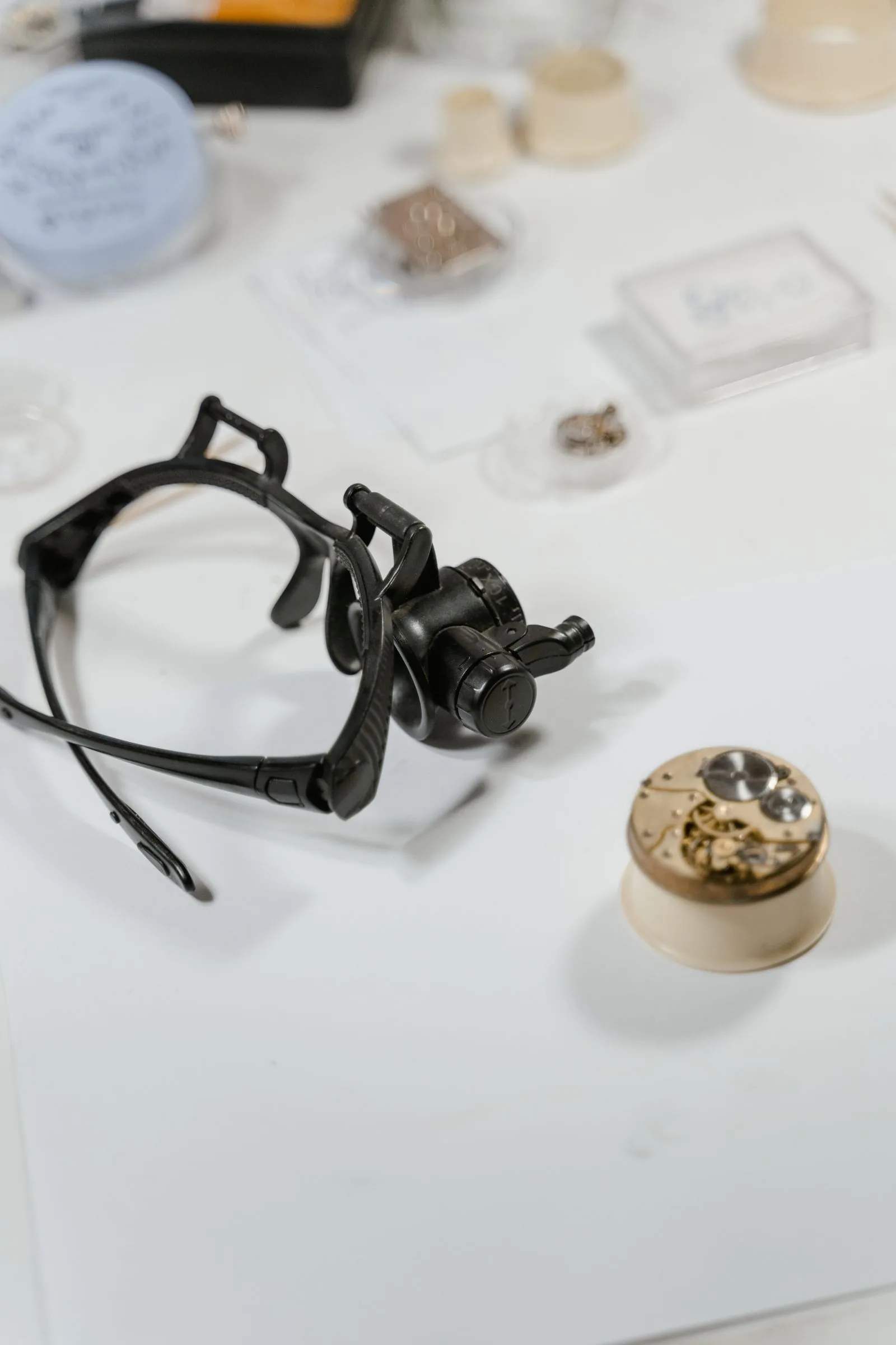 Watchmaker's head-mounted loupe beside a movement on a white bench, used to check a pre-owned Rolex before you pay