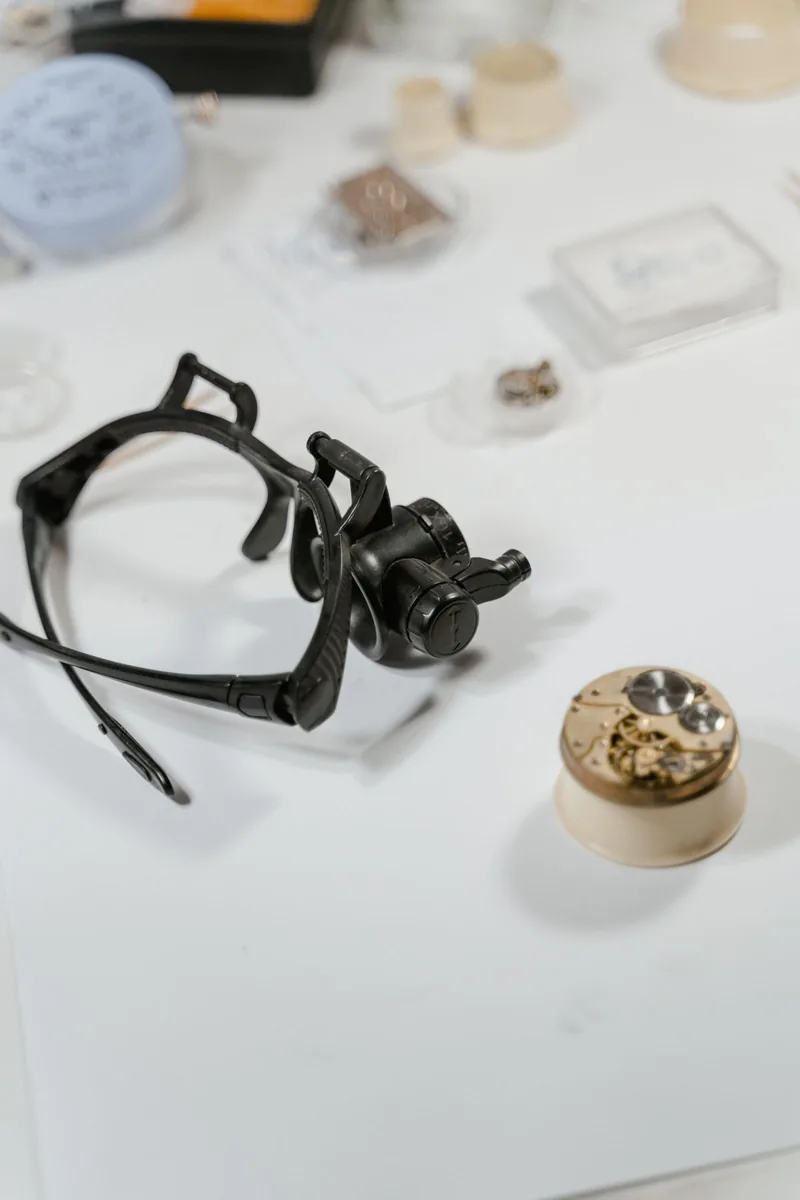 Watchmaker's head-mounted loupe beside a movement on a white bench