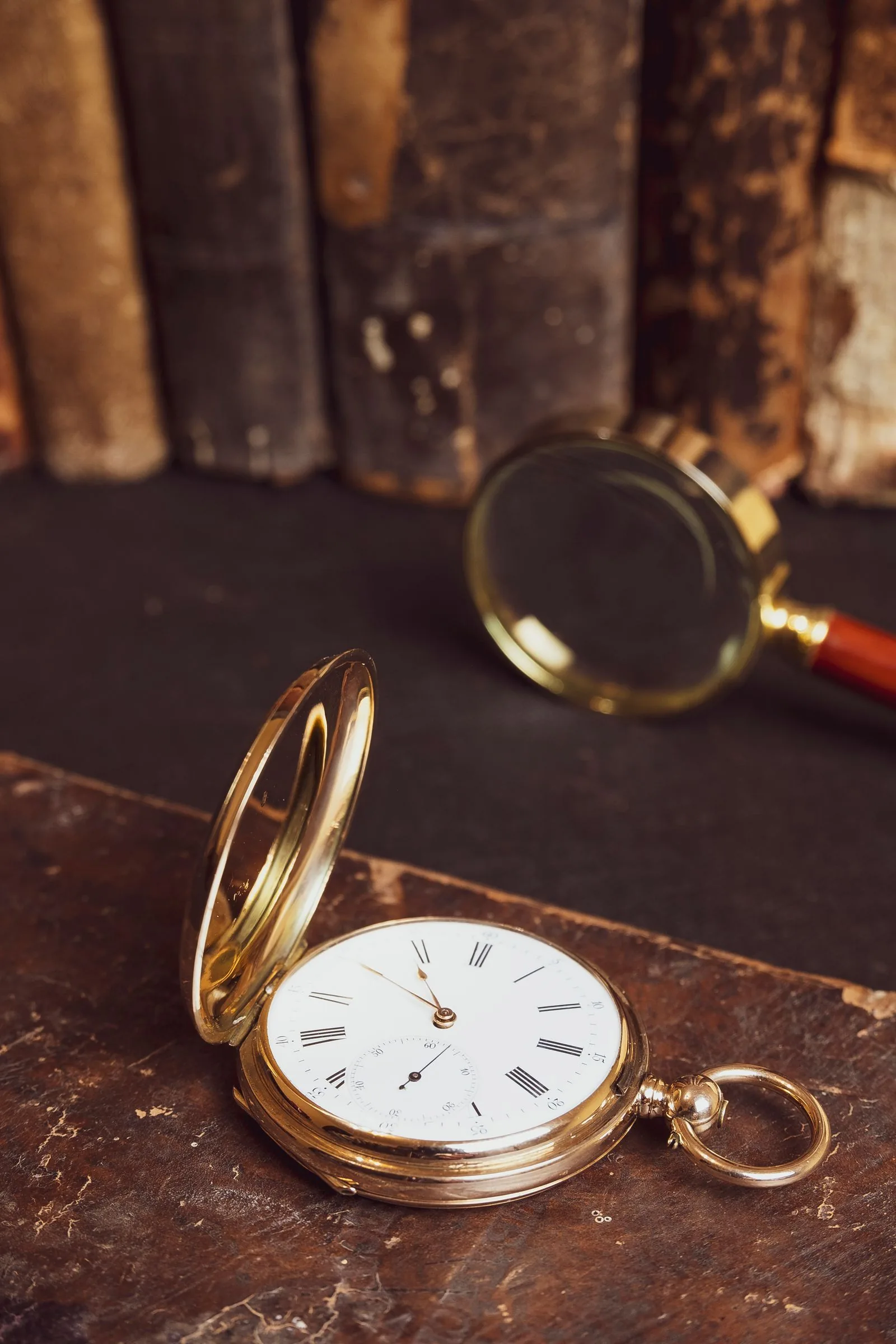 Magnifying glass and an open pocket watch on a dark surface, for reading numbers when buying a used Rolex
