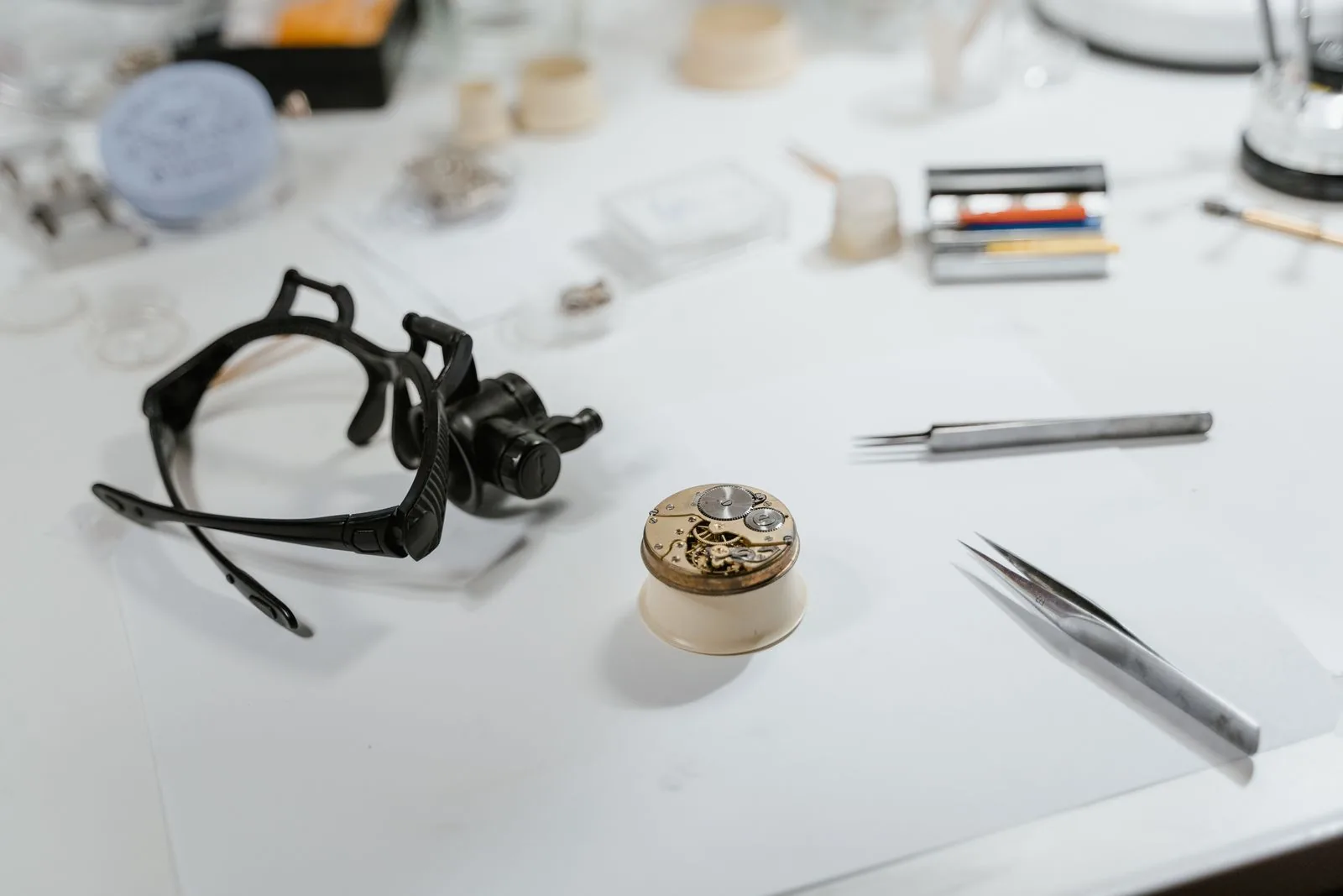 Watchmaker's head loupe, tweezers and a movement on a white bench; get an expert view when buying from a private seller