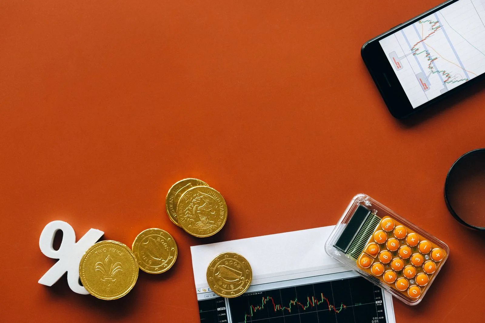 Coins, a small calculator and a percentage sign on a grey surface, for adding up the total repayable on Rolex finance
