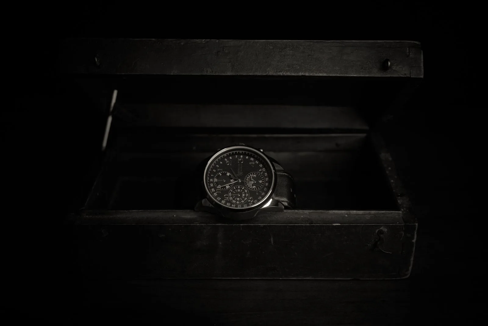 Wristwatch resting in an open dark wooden box in low light, as this watch storage guide suggests for a collection at home