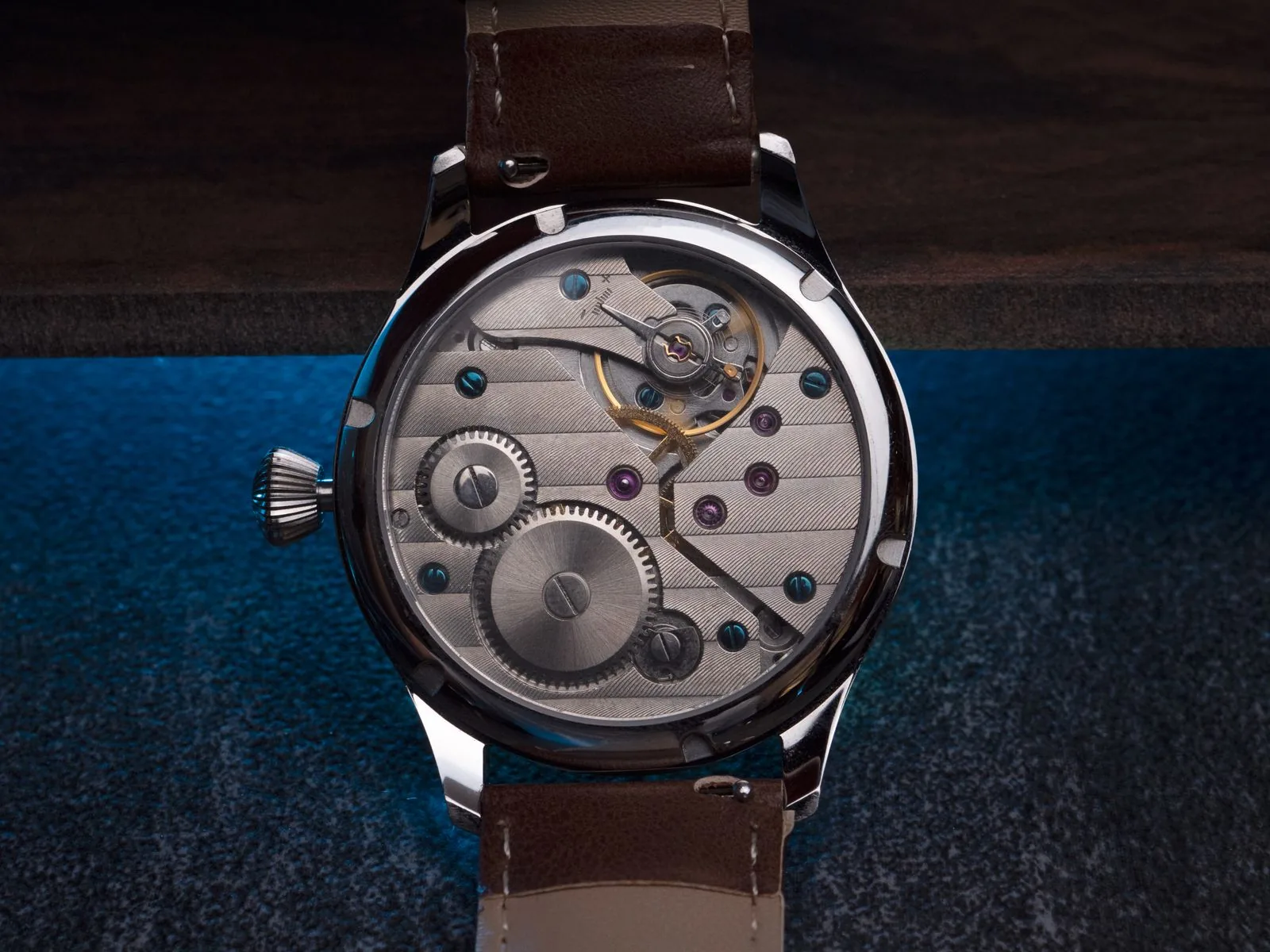 Wristwatch on dark leather showing a transparent caseback and manual-wind movement; a transparent caseback, the movement a watch warranty covers
